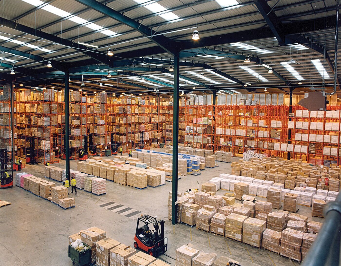 A modern warehouse with tall pallet racking and a forklift working in the aisle