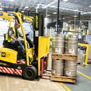 person driving yellow forklift carrying metal barrels